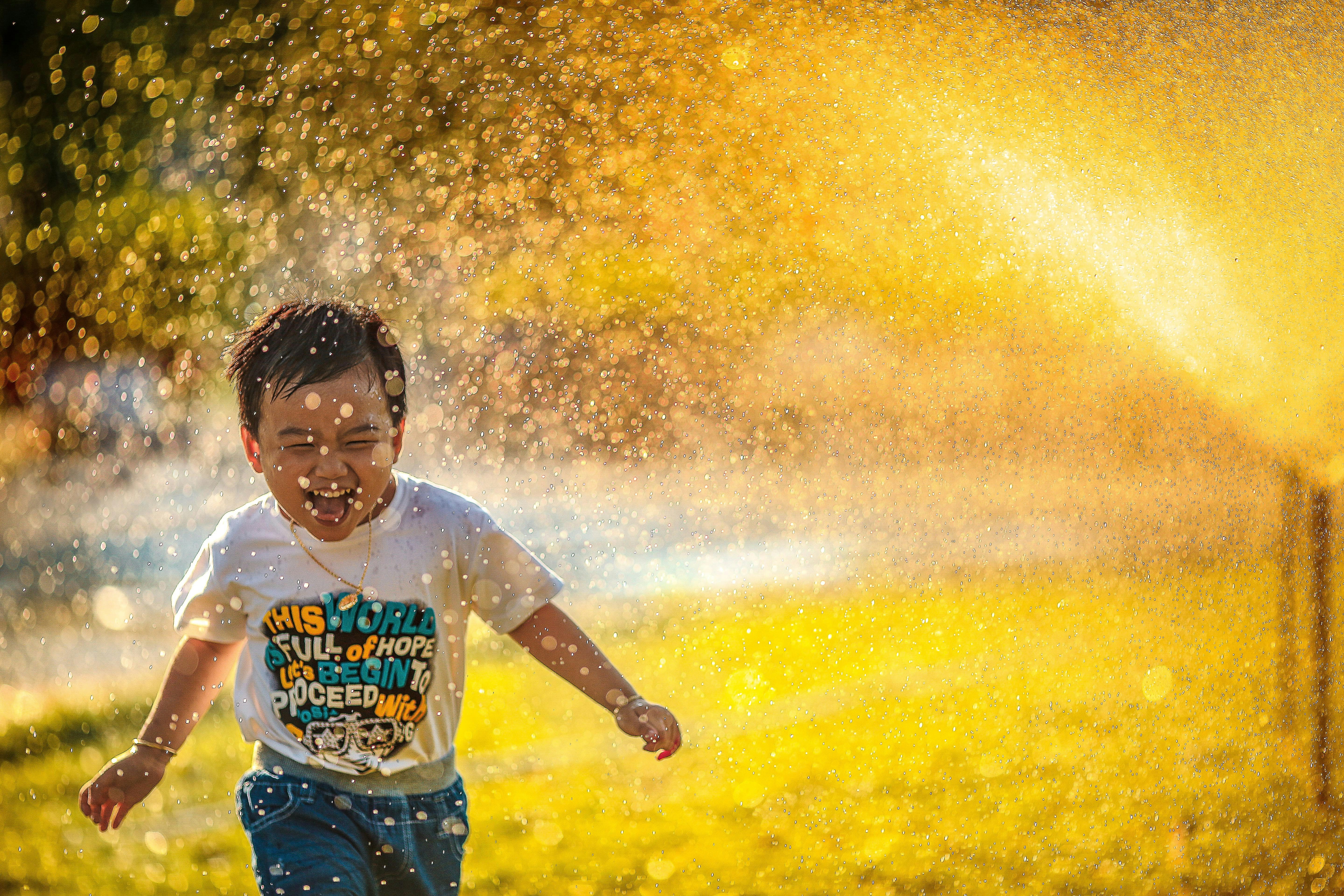 A child joyfully running through the sprinklers outside